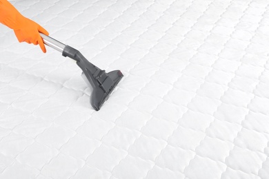 Photo of Person disinfecting mattress with vacuum cleaner, closeup. Space for text
