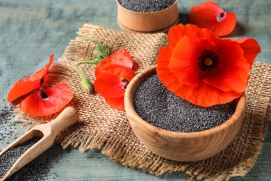 Wooden bowl of poppy seeds, scoop and flowers on color table