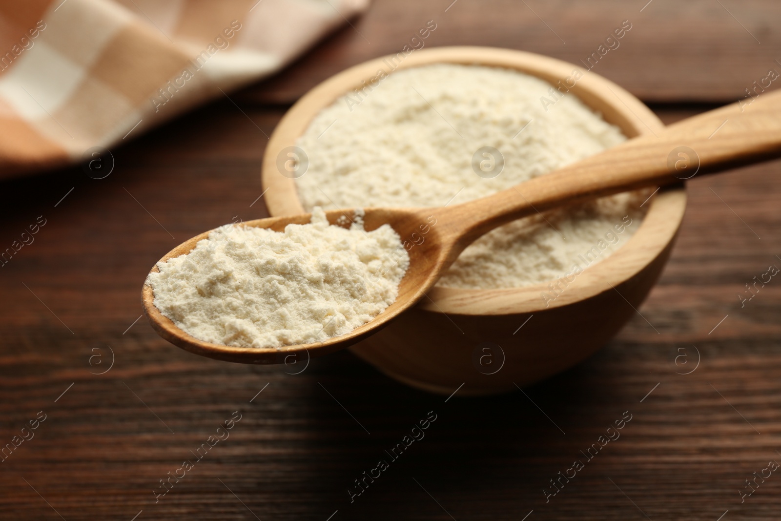 Photo of Baking powder in bowl and spoon on wooden table, closeup