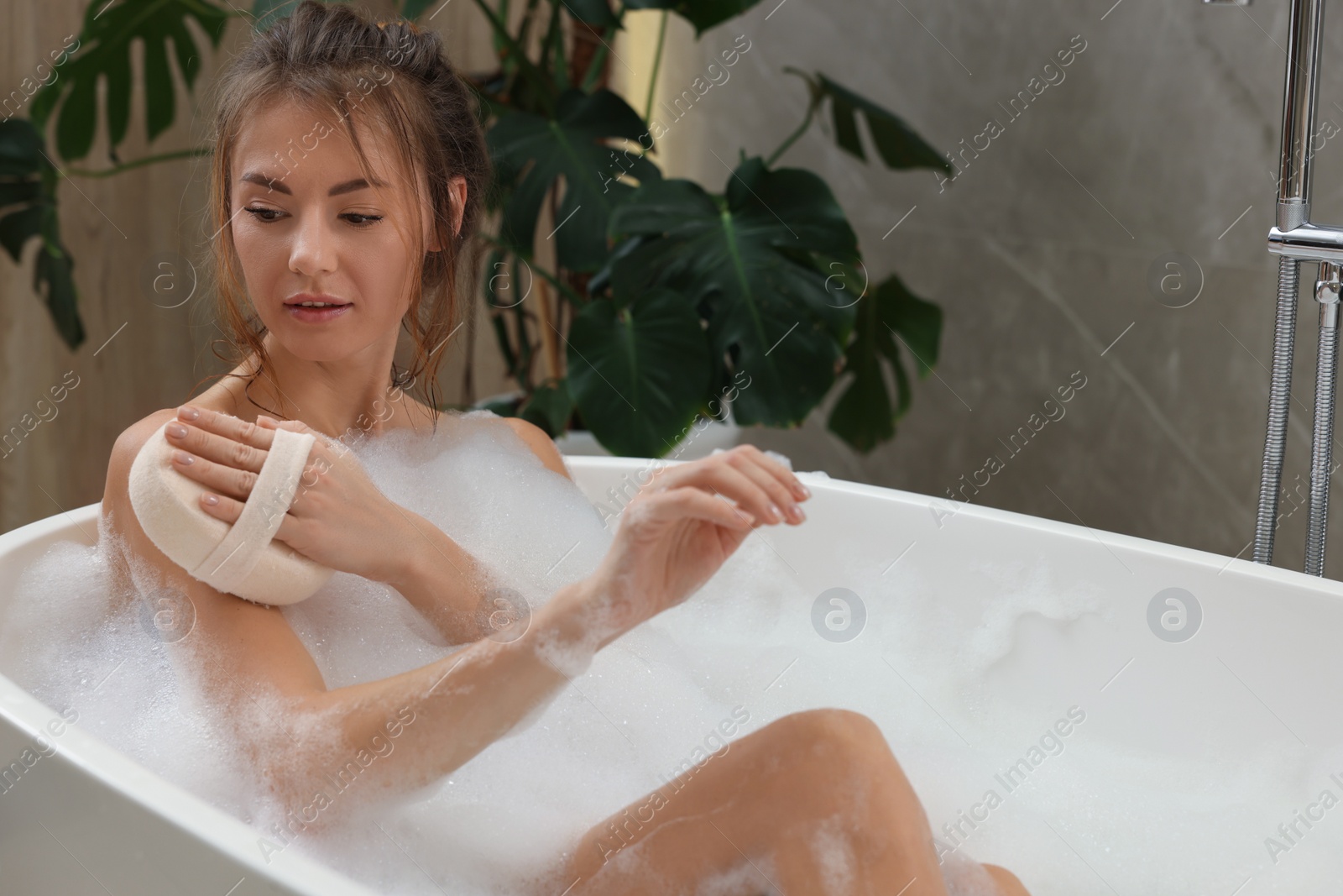 Photo of Beautiful woman with sponge taking bath indoors, space for text