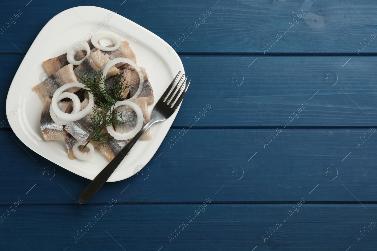 Photo of Plate with sliced salted herring fillet, onion rings and dill on blue wooden table, top view. Space for text