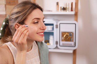 Woman using cosmetic product and mini fridge indoors, space for text