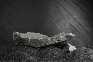 Photo of Presentation of product. Stone podium on black sand against dark textured background. Space for text