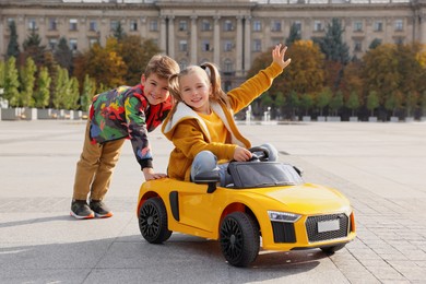Photo of Cute boy pushing children's car with little girl outdoors on sunny day
