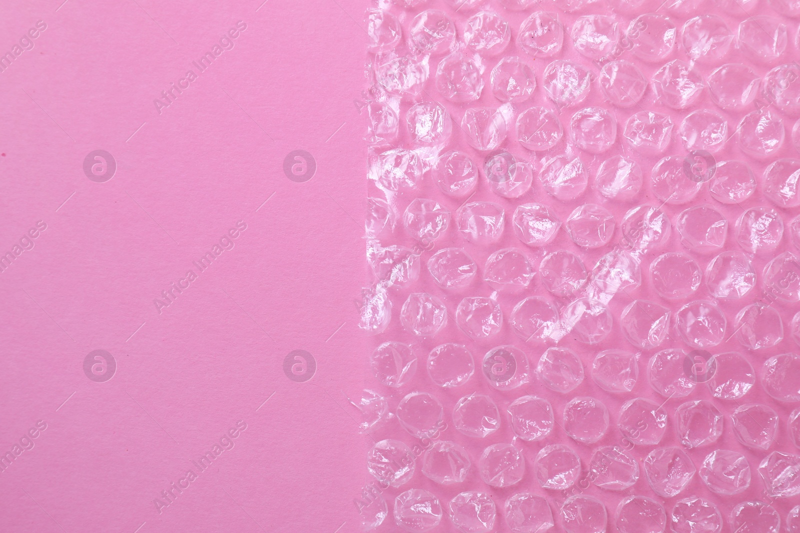 Photo of Transparent bubble wrap on pink background, top view. Space for text