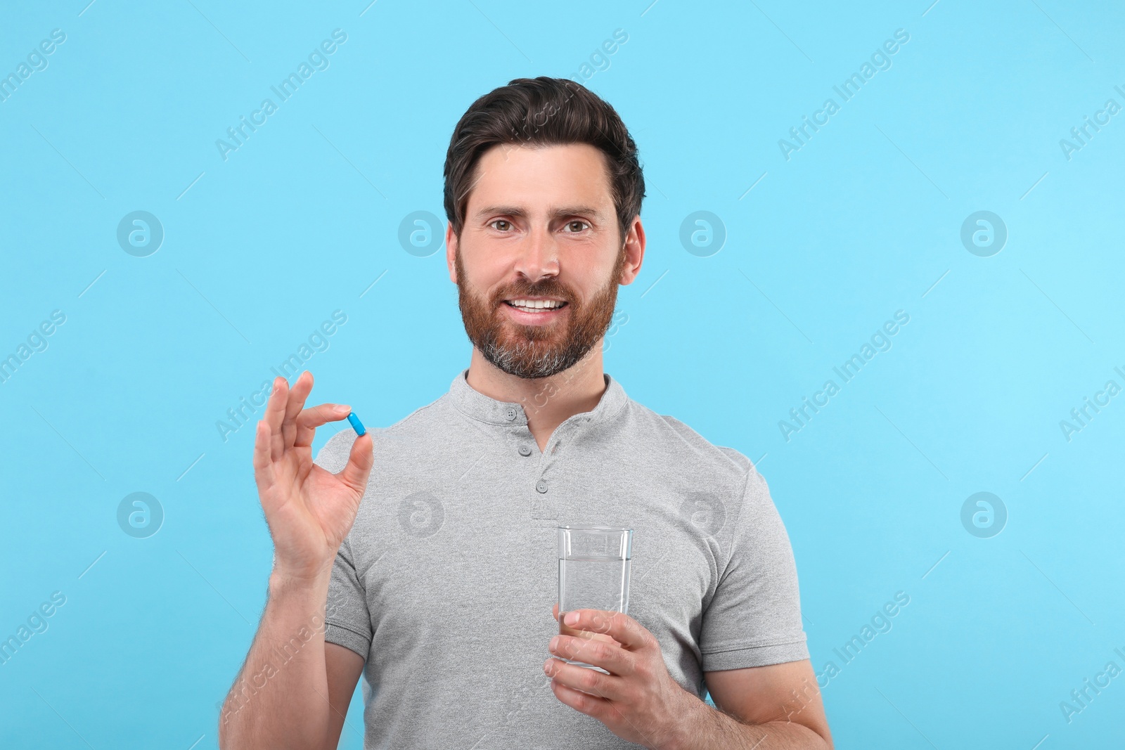 Photo of Handsome man with glass of water and pill on light blue background