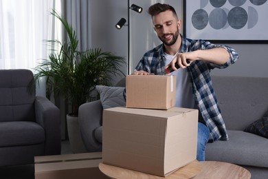 Photo of Man using utility knife to open parcel at home