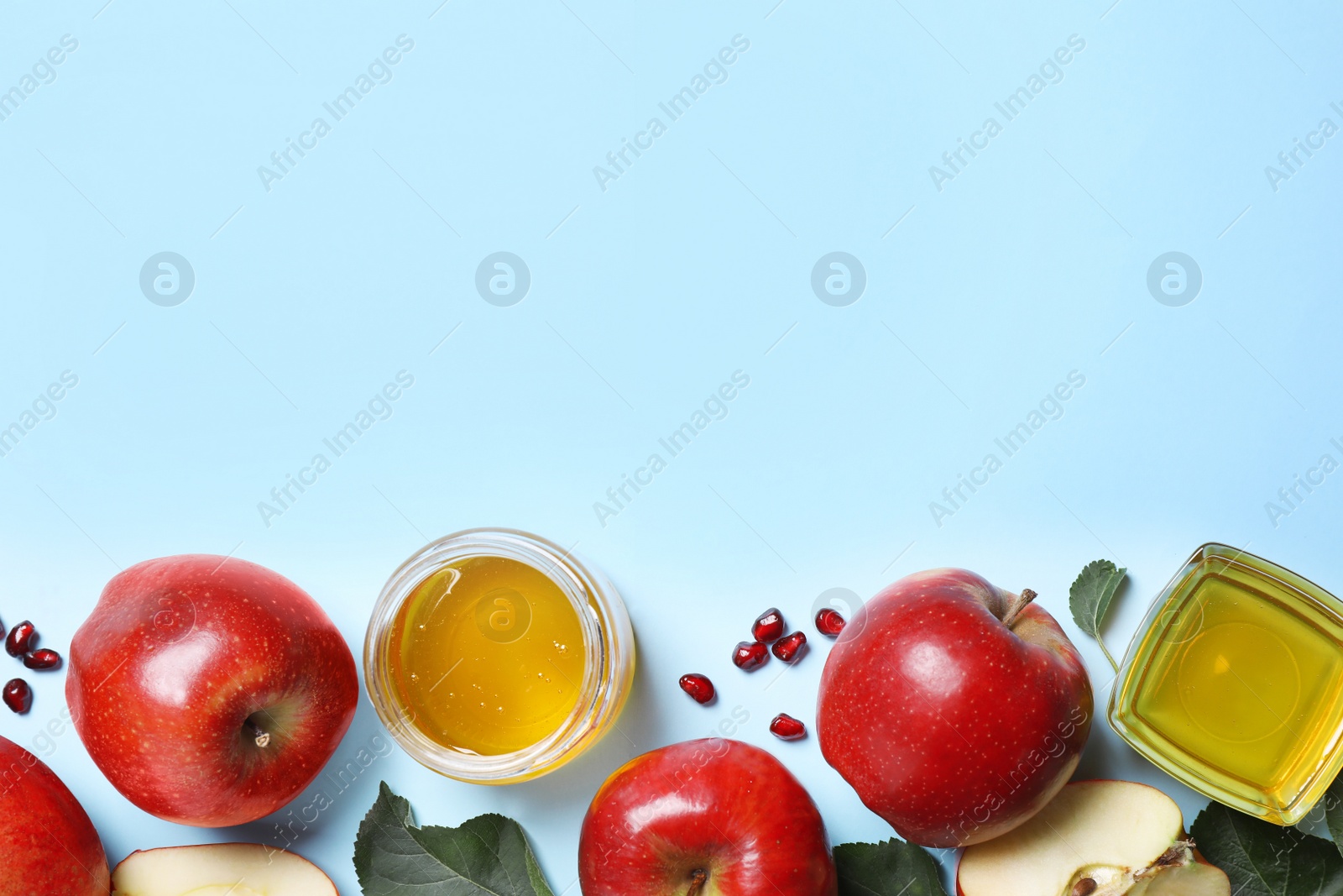 Photo of Honey, apples and pomegranates on light blue background, flat lay with space for text. Rosh Hashanah holiday