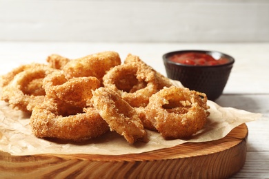 Homemade crunchy fried onion rings with tomato sauce on wooden table, closeup