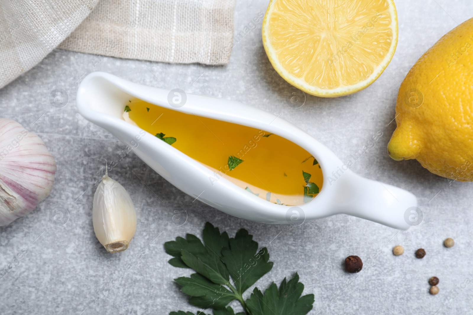 Photo of Ceramic boat with lemon sauce and ingredients on light grey table, flat lay. Delicious salad dressing