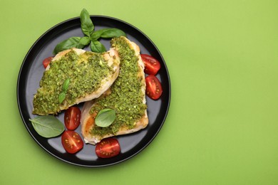 Photo of Delicious chicken breasts with pesto sauce, tomatoes and basil on light green table, top view. Space for text