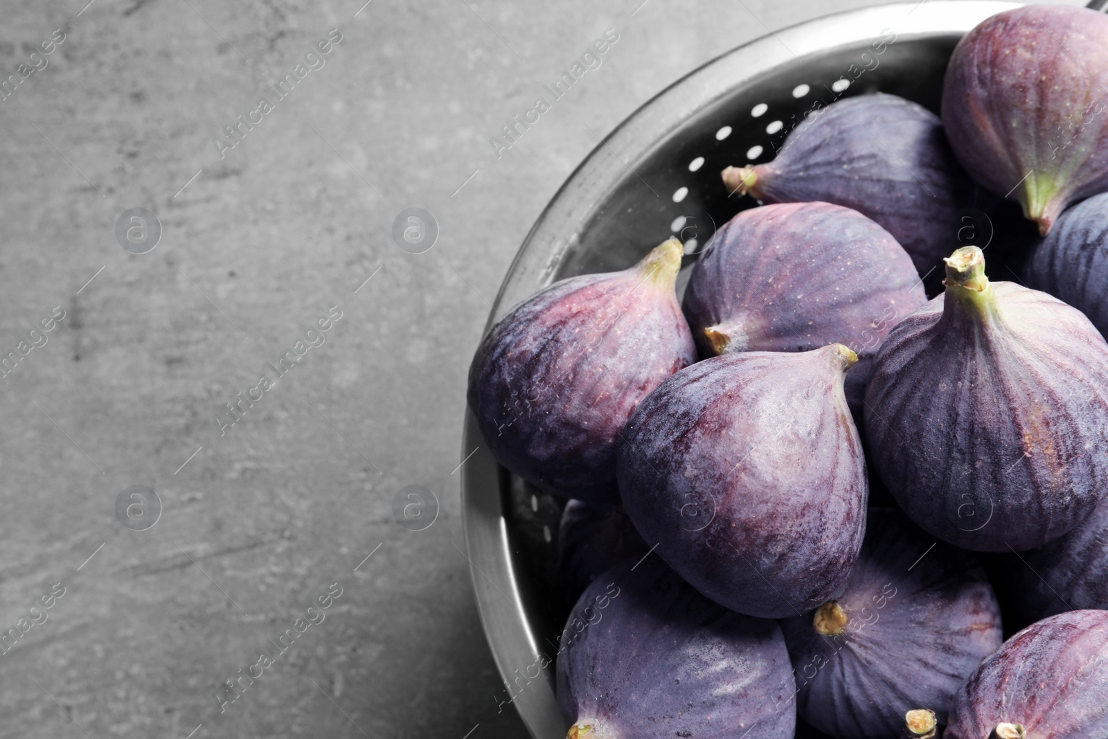 Photo of Colander with fresh ripe figs on gray background, top view. Space for text