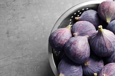 Colander with fresh ripe figs on gray background, top view. Space for text