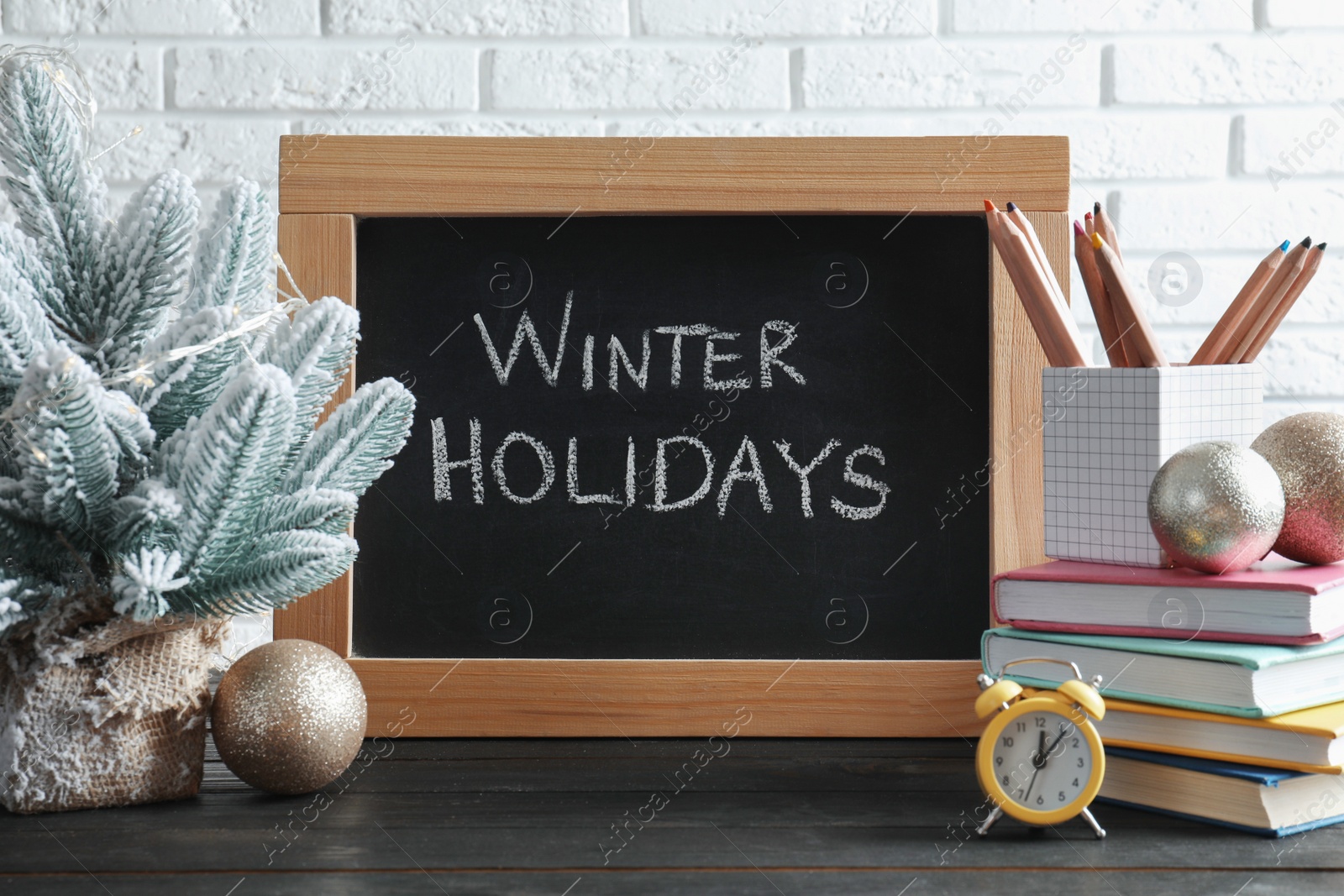 Photo of Chalkboard with phrase Winter Holidays, Christmas decor and stationery on black wooden table near white brick wall