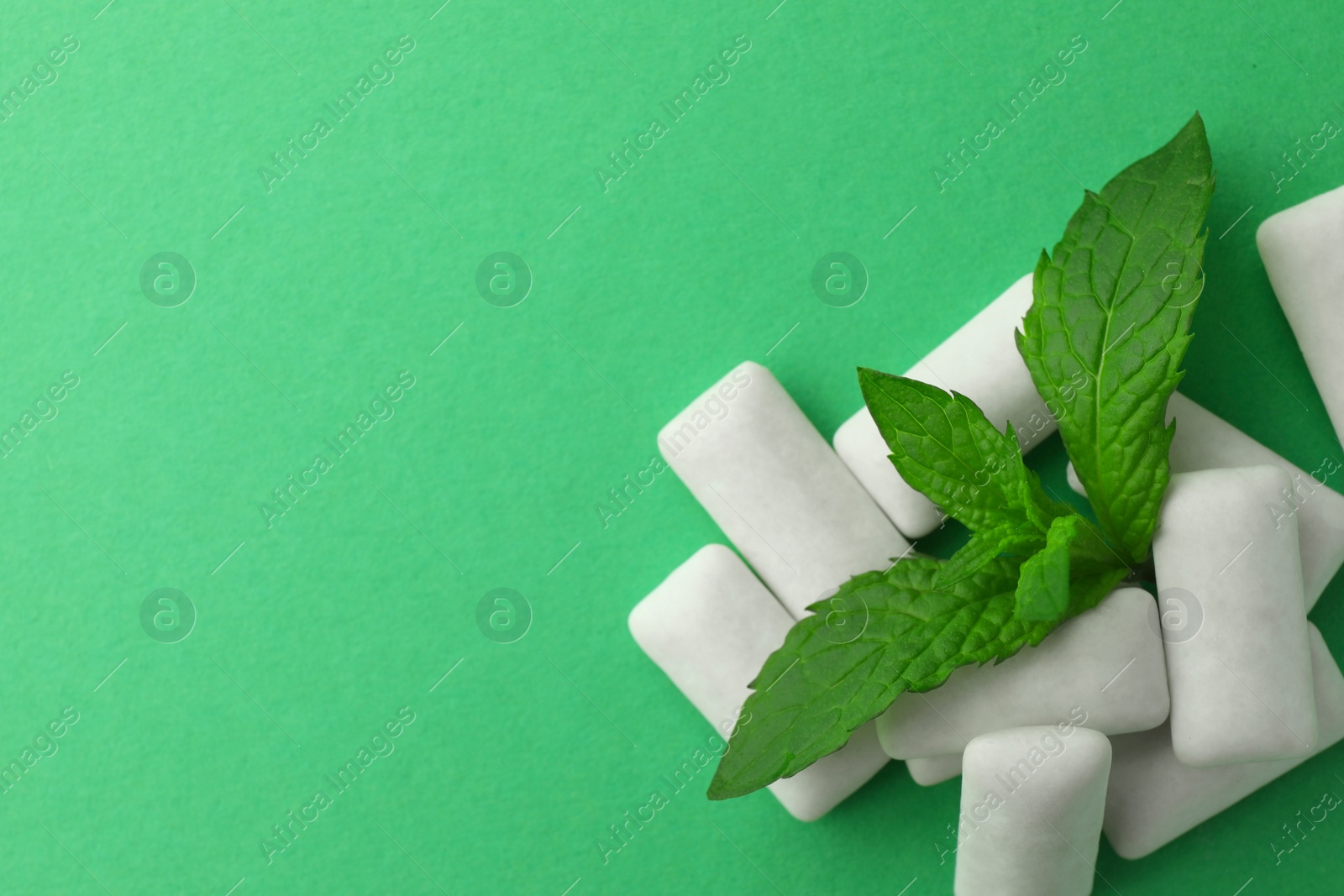 Photo of Tasty white chewing gums and mint leaves on green background, top view. Space for text