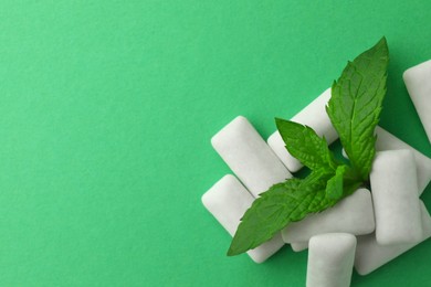 Tasty white chewing gums and mint leaves on green background, top view. Space for text