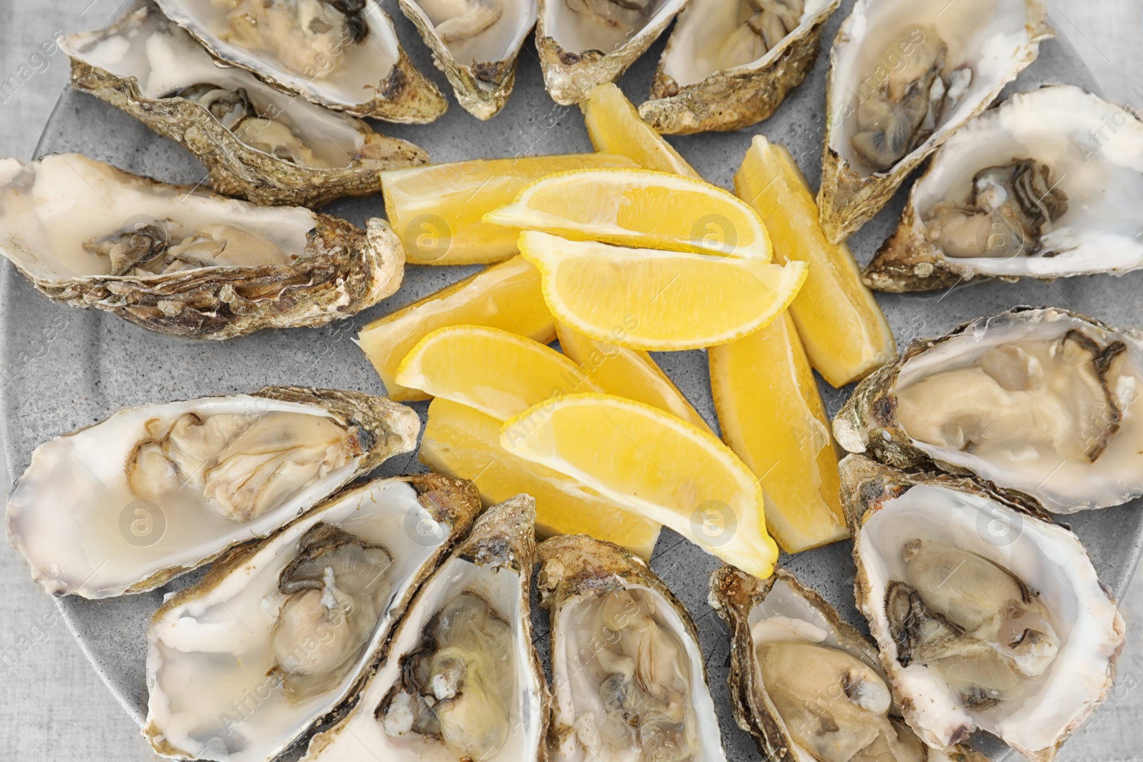 Photo of Top view of fresh oysters with cut juicy lemon on plate, closeup