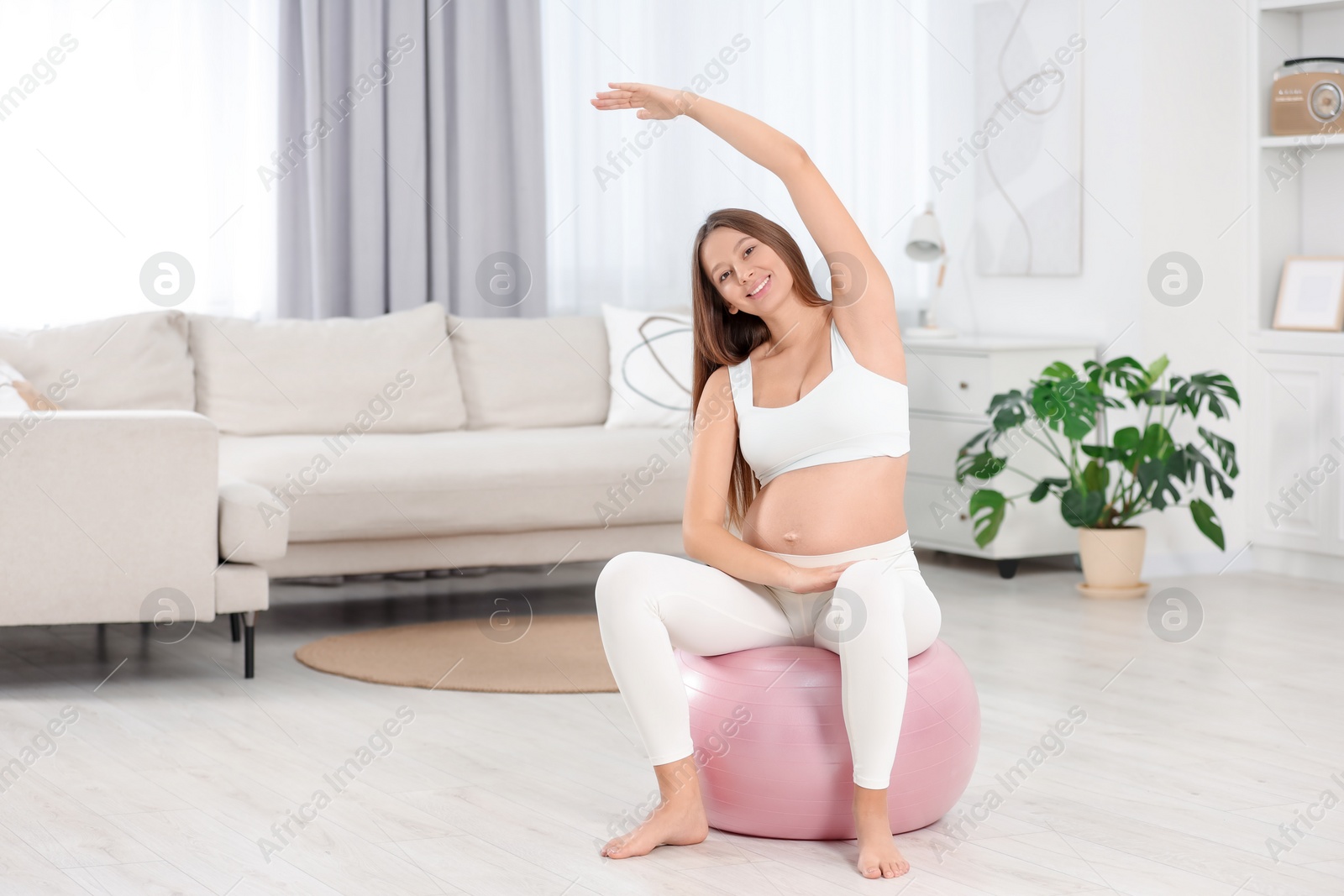 Photo of Pregnant woman doing exercises on fitness ball in room, space for text. Home yoga