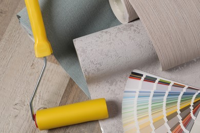 Photo of Wall paper rolls, color palette and tool on wooden floor, above view