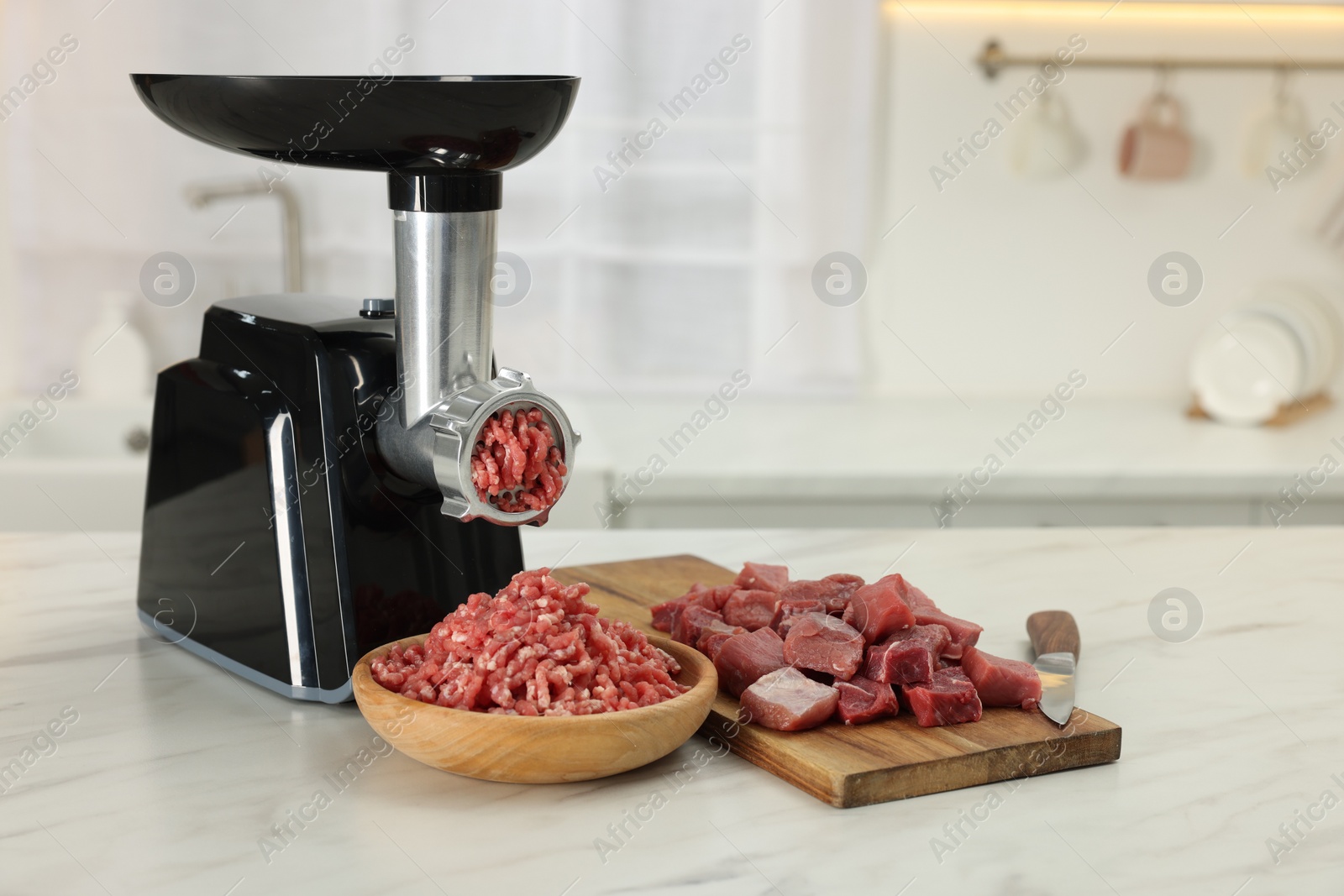 Photo of Electric meat grinder with beef on white marble table in kitchen