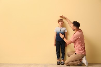 Photo of Father measuring height of his son near beige wall indoors. Space for text