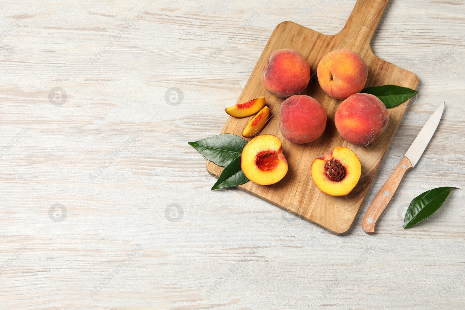 Photo of Fresh ripe peaches with green leaves and knife on light wooden table, top view. Space for text