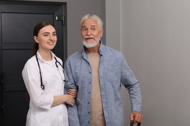 Photo of Young healthcare worker assisting senior man indoors. Space for text