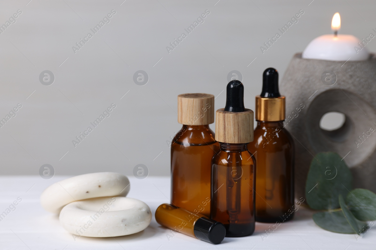 Photo of Different aromatherapy products, burning candle and eucalyptus leaves on white wooden table against light background, space for text