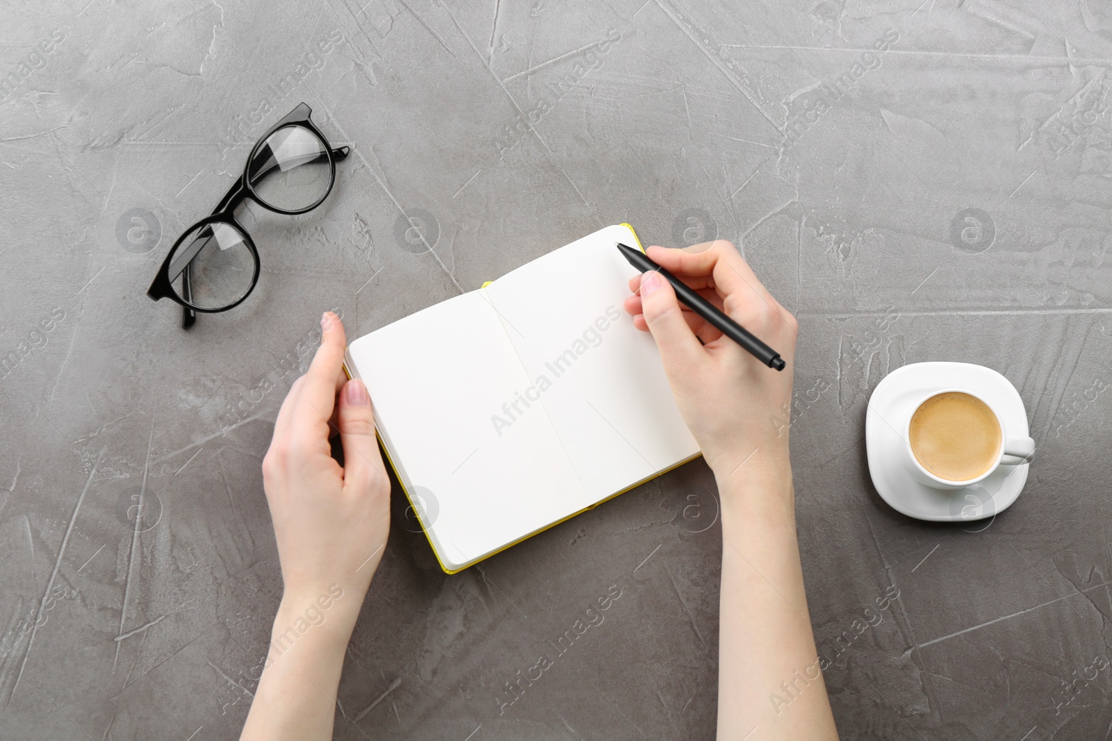 Photo of Woman writing in notebook at grey table, top view