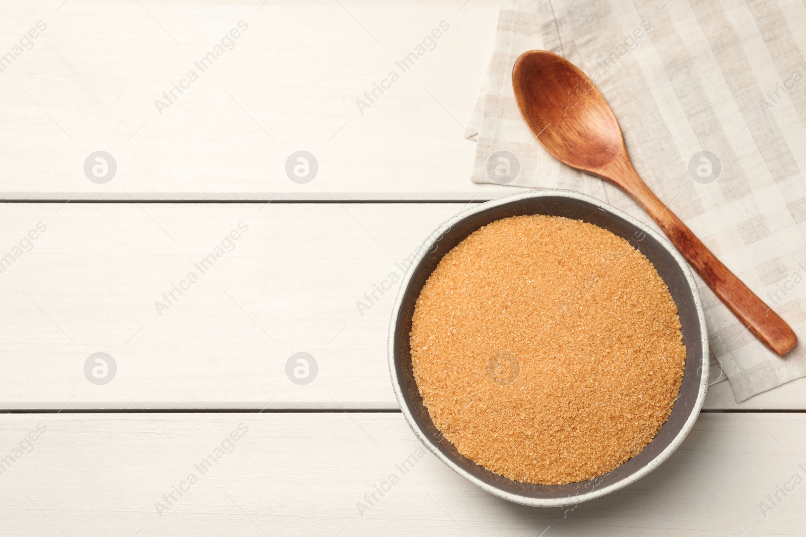 Photo of Bowl of brown sugar, spoon and napkin on white wooden table, flat lay. Space for text