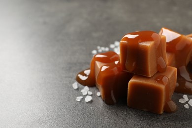 Photo of Yummy caramel candies with sauce and sea salt on grey table, closeup. Space for text