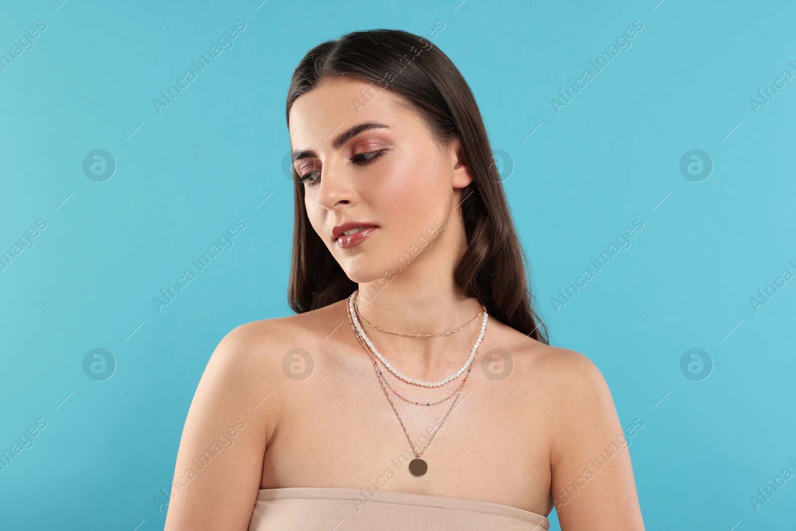 Photo of Beautiful woman with elegant necklaces on light blue background