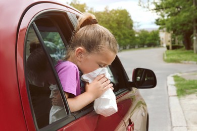 Photo of Little girl with paper bag suffering from nausea in car