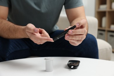 Diabetes test. Man checking blood sugar level with lancet pen at white table, closeup