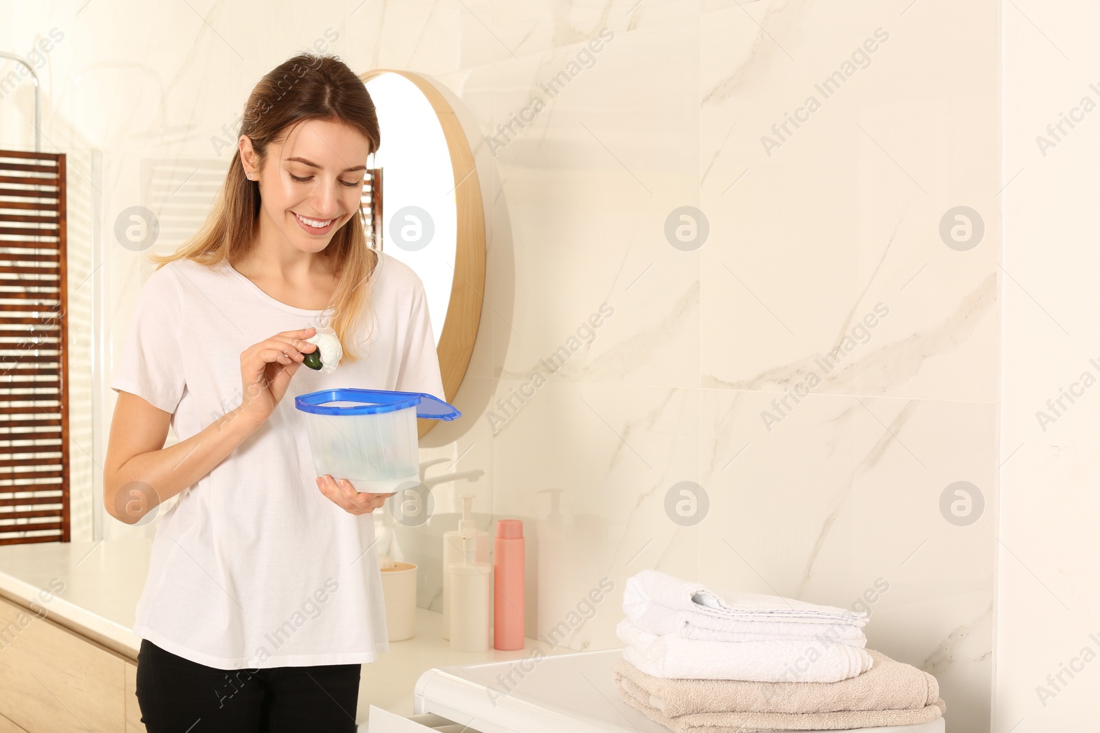 Photo of Woman holding container with laundry detergent capsules in bathroom