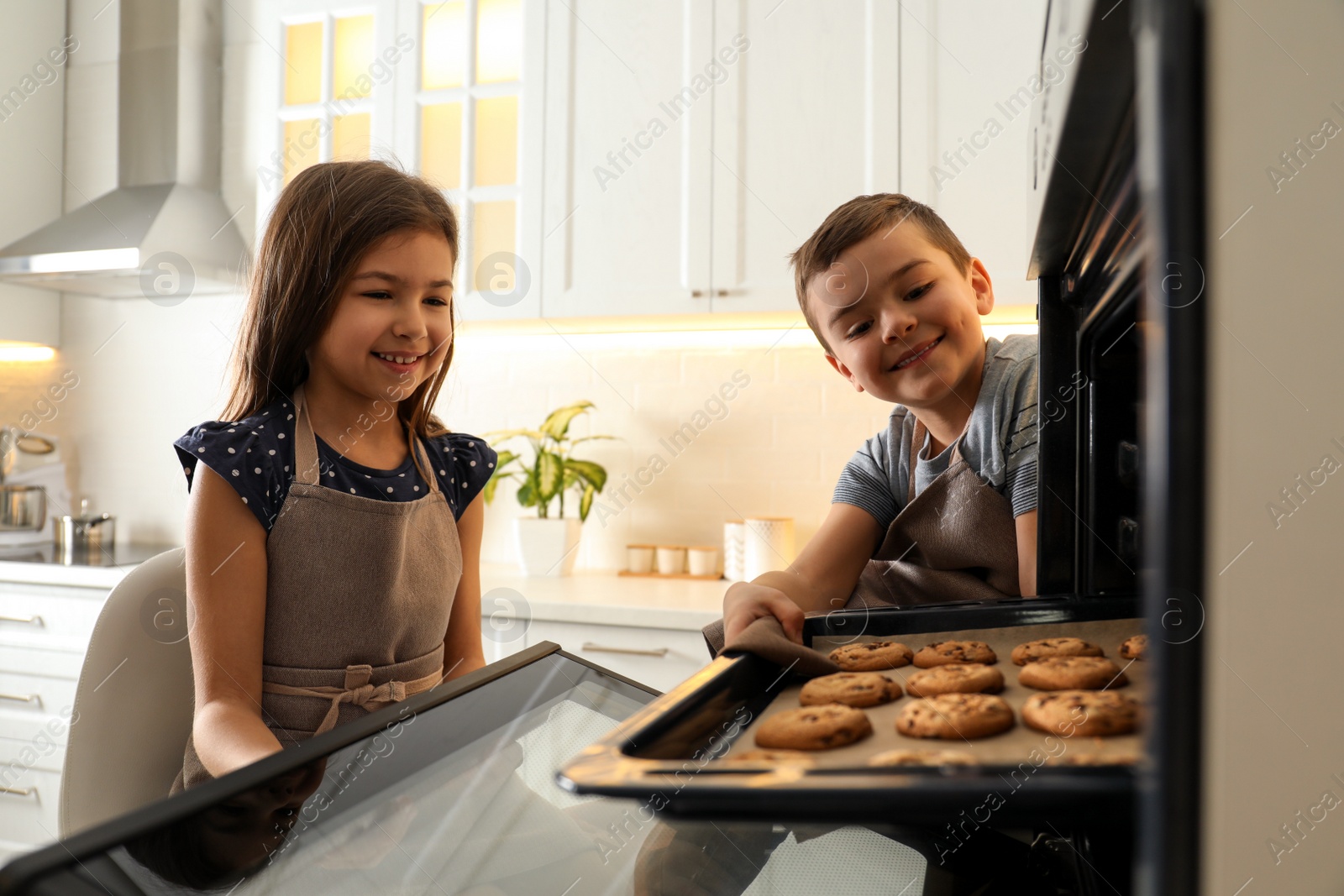 Photo of Cute little children taking cookies out of oven in kitchen. Cooking pastry