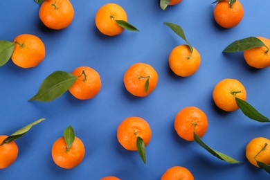 Fresh tangerines with green leaves on blue background, flat lay