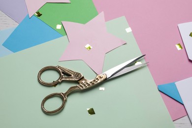 Pair of scissors with colorful paper sheets on white wooden table, above view