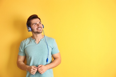 Photo of Handsome man with headphones enjoying music on color background. Space for text