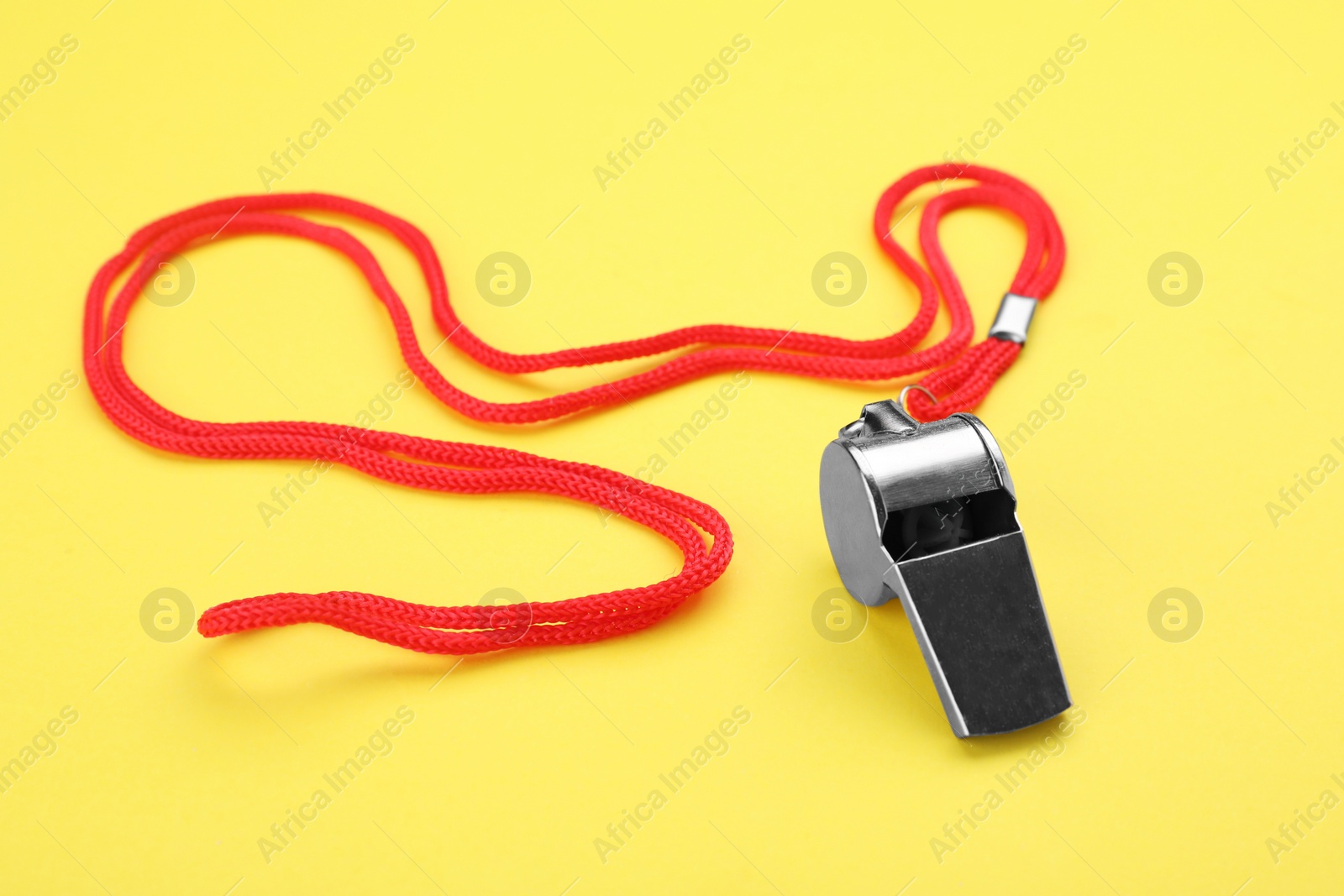 Photo of One metal whistle with red cord on yellow background