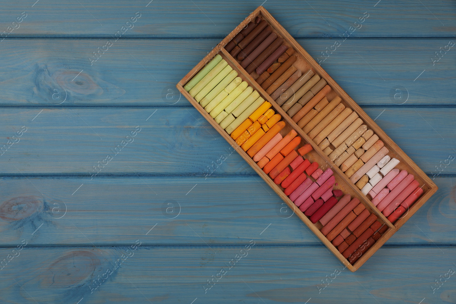 Photo of Drawing pastel set in box on light blue wooden background, top view. Space for text