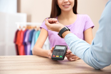 Man using terminal for contactless payment with smart watch in shop, closeup