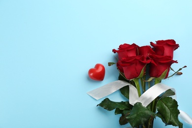 Beautiful red roses, white ribbon and decorative heart on light blue background, flat lay with space for text. Valentine's Day celebration