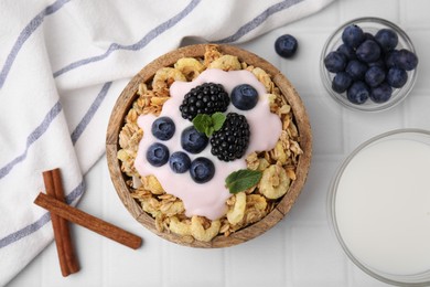 Tasty granola, yogurt and fresh berries in bowl on white tiled table, flat lay. Healthy breakfast