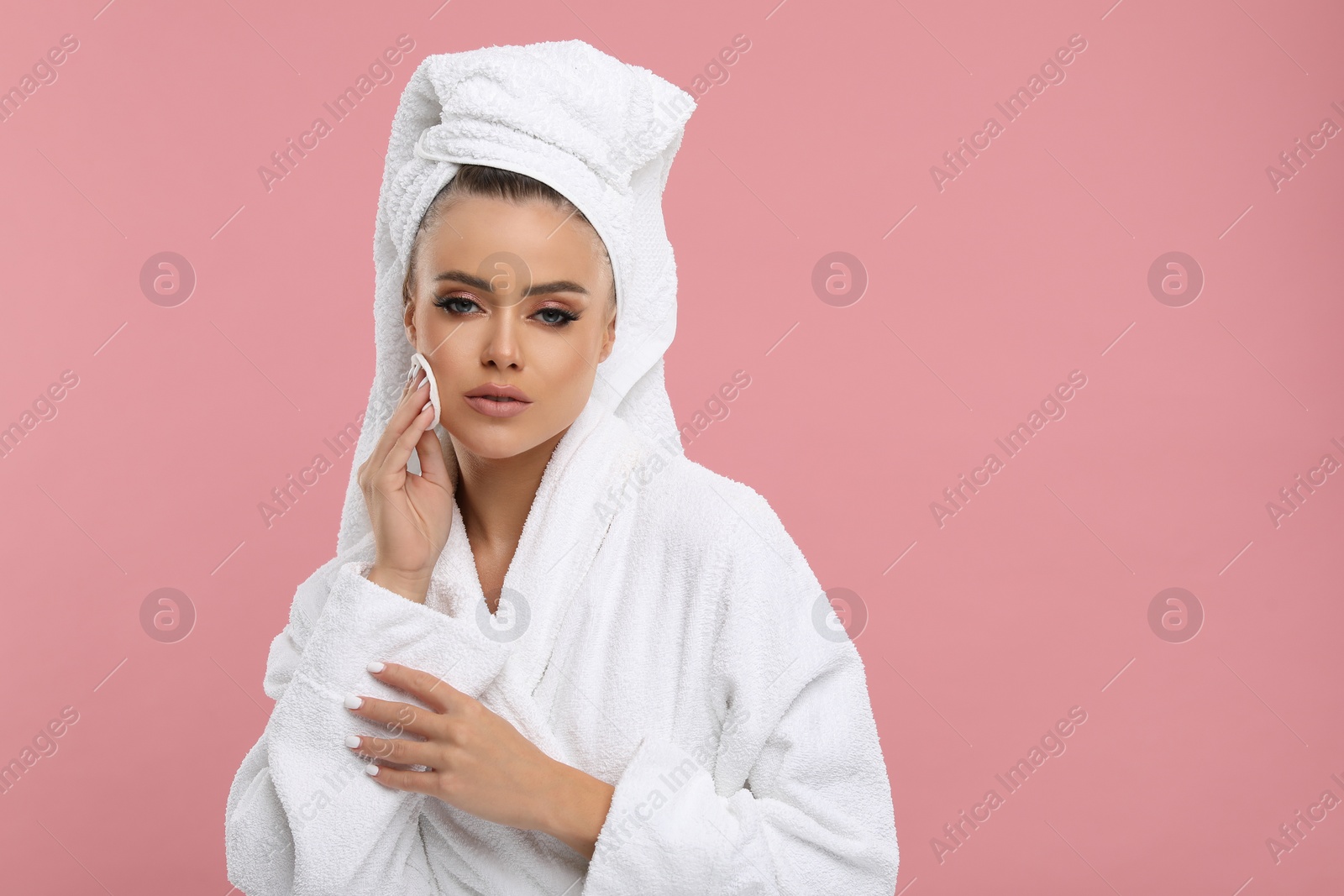 Photo of Beautiful woman removing makeup with cotton pad on pink background, space for text