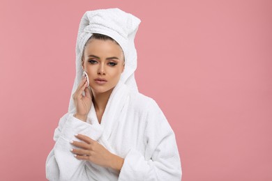 Beautiful woman removing makeup with cotton pad on pink background, space for text