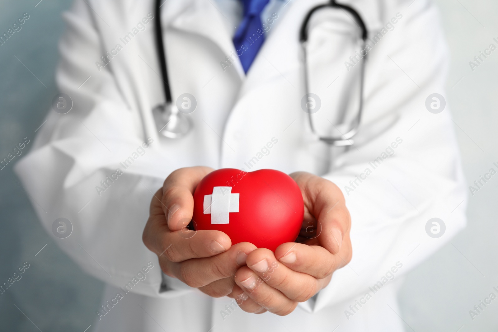 Photo of Doctor holding red heart with adhesive plasters, closeup view. Cardiology concept