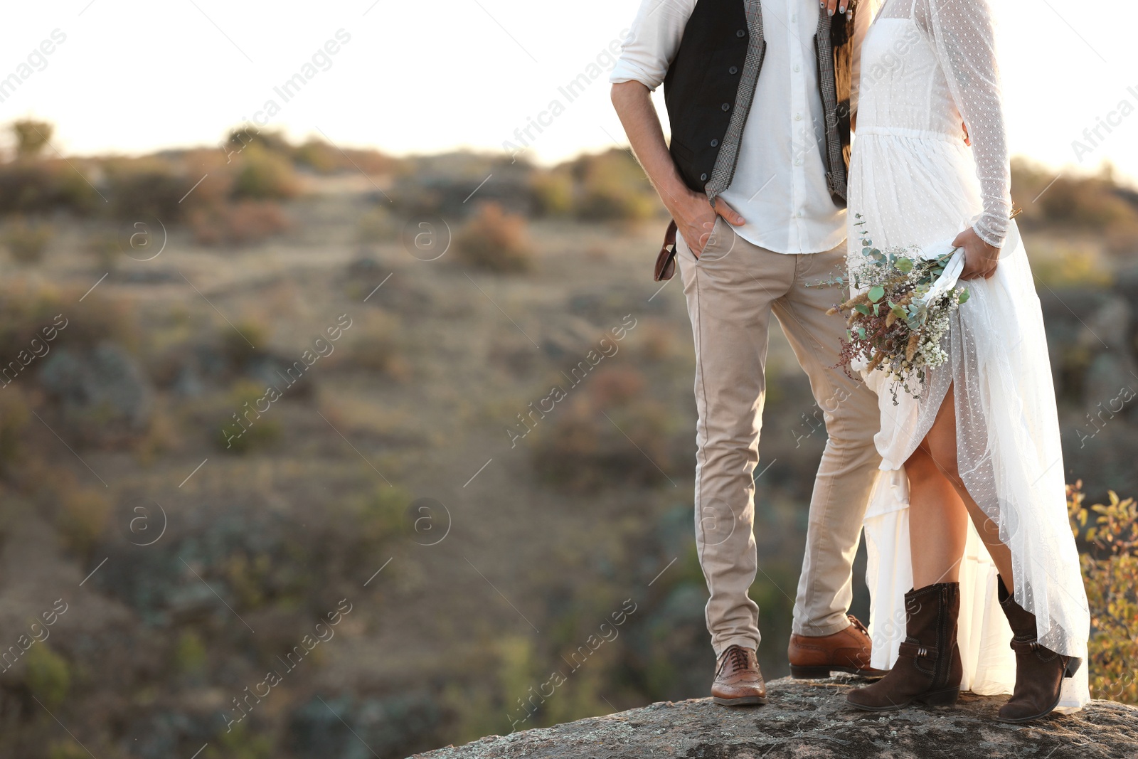 Photo of Happy newlyweds with beautiful field bouquet standing on rock outdoors, closeup