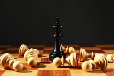 King among fallen white chess pieces on wooden board against dark background. Competition concept