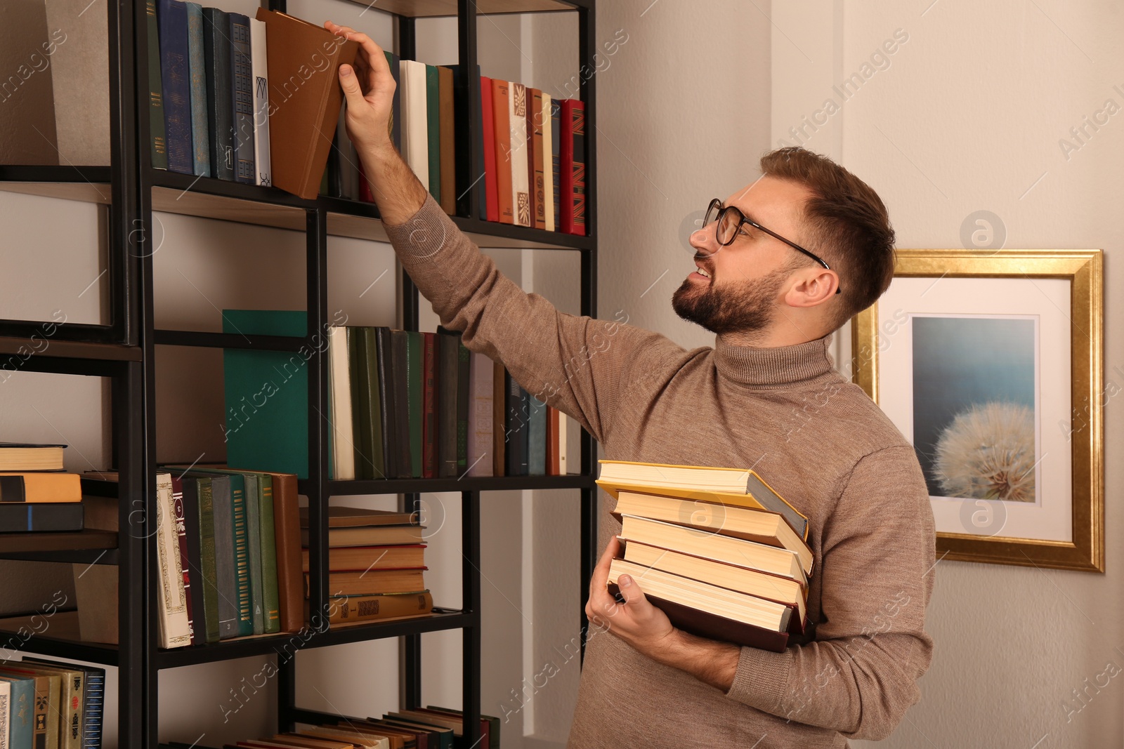 Photo of Young man choosing books on shelf in home library